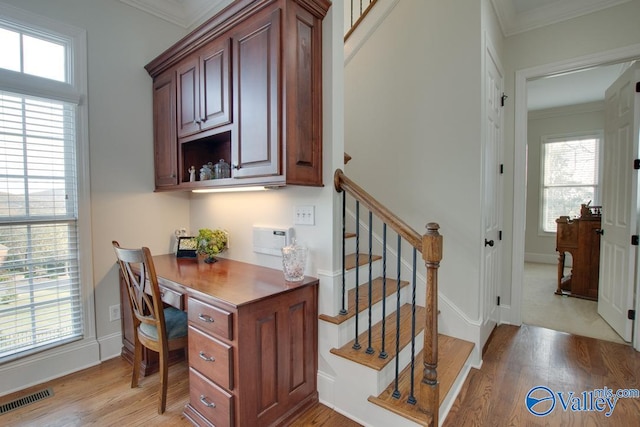 home office featuring light wood-type flooring, a wealth of natural light, built in desk, and ornamental molding