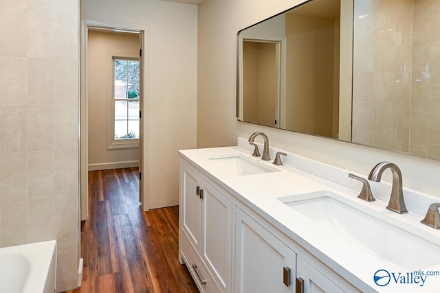 bathroom featuring double vanity, wood finished floors, a sink, and a washtub