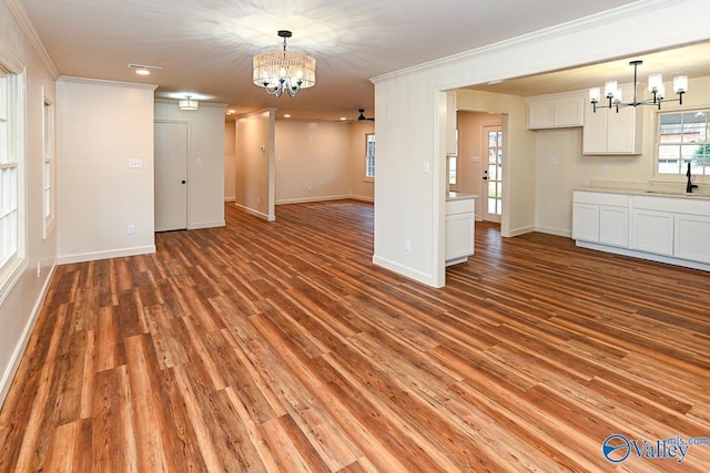 unfurnished living room with a chandelier, light wood-style floors, a sink, and crown molding