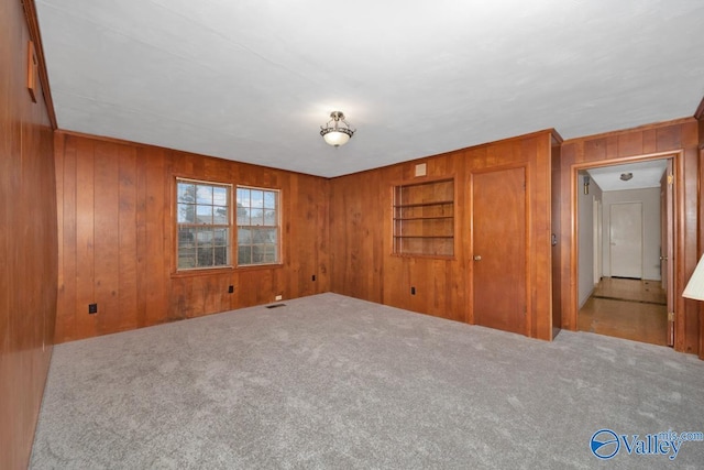 carpeted spare room featuring built in shelves and wood walls