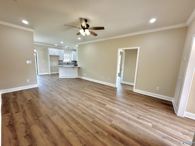 unfurnished living room with baseboards, light wood-style floors, ornamental molding, and a ceiling fan