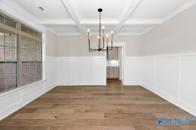 unfurnished dining area featuring coffered ceiling, beam ceiling, a chandelier, and hardwood / wood-style floors