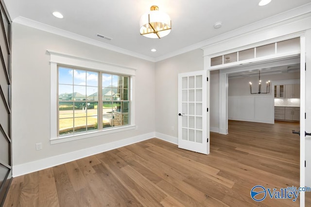 empty room featuring french doors, ornamental molding, hardwood / wood-style floors, and a notable chandelier