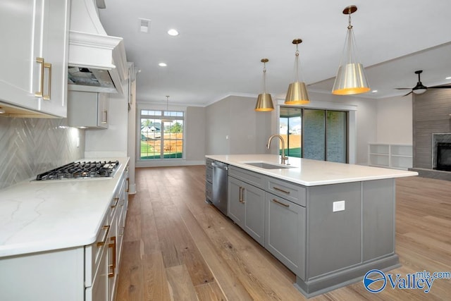 kitchen with appliances with stainless steel finishes, tasteful backsplash, an island with sink, sink, and hanging light fixtures