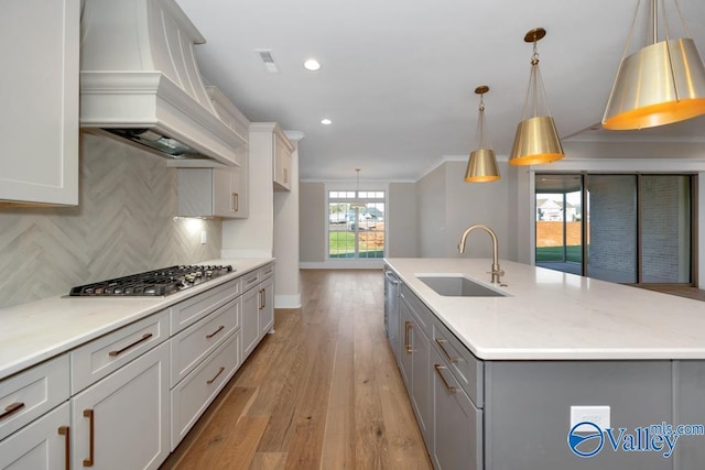 kitchen with sink, hanging light fixtures, tasteful backsplash, custom range hood, and stainless steel gas cooktop