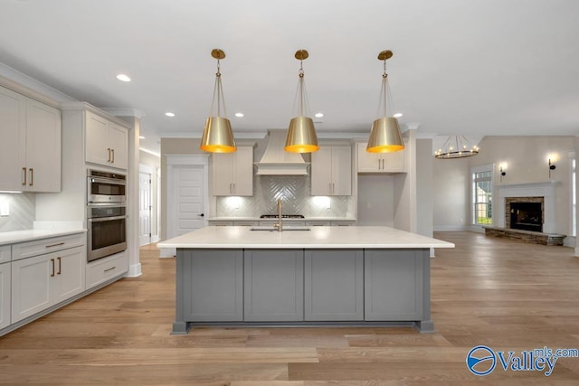 kitchen with custom exhaust hood, a center island with sink, and backsplash