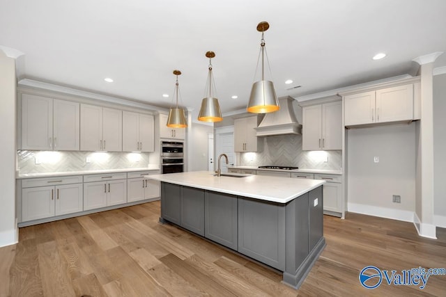 kitchen featuring sink, gas cooktop, a kitchen island with sink, hanging light fixtures, and custom exhaust hood