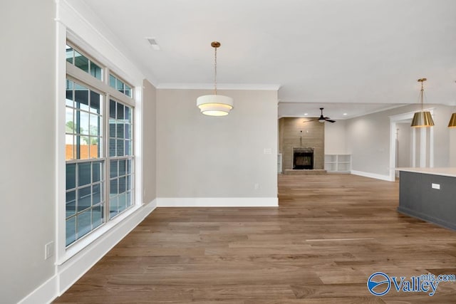 interior space with a tile fireplace, wood-type flooring, ornamental molding, and ceiling fan