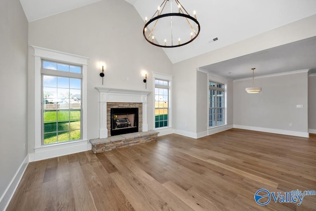 unfurnished living room featuring an inviting chandelier, a stone fireplace, wood-type flooring, and high vaulted ceiling