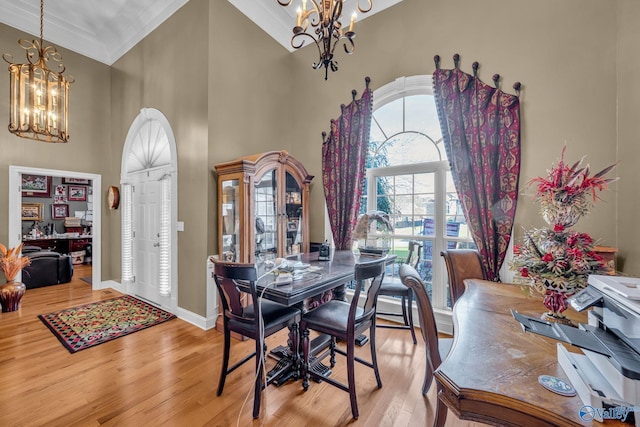 dining room featuring a notable chandelier, ornamental molding, a high ceiling, and light hardwood / wood-style flooring