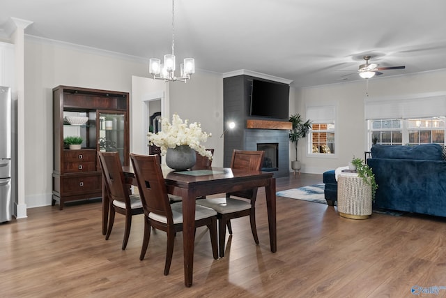 dining space with ornamental molding, a fireplace, light wood finished floors, and ceiling fan with notable chandelier