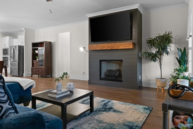 living room featuring a large fireplace, baseboards, ornamental molding, and wood finished floors