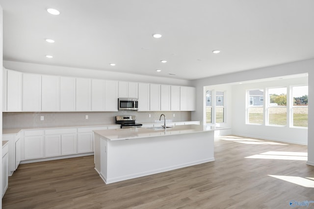 kitchen with stainless steel appliances, white cabinetry, sink, and a kitchen island with sink