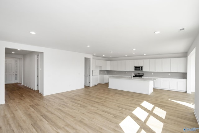 kitchen with sink, white cabinetry, light wood-type flooring, appliances with stainless steel finishes, and a kitchen island with sink