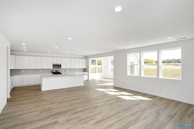 kitchen with white cabinetry, appliances with stainless steel finishes, a wealth of natural light, and a center island with sink