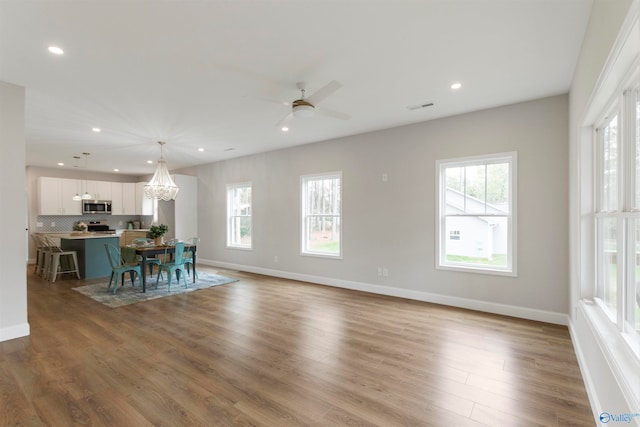 unfurnished dining area with hardwood / wood-style floors and ceiling fan with notable chandelier