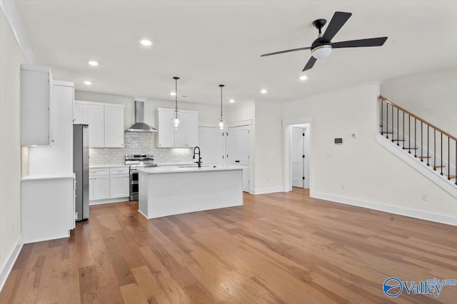 kitchen with stainless steel appliances, tasteful backsplash, light wood-style flooring, a sink, and wall chimney range hood