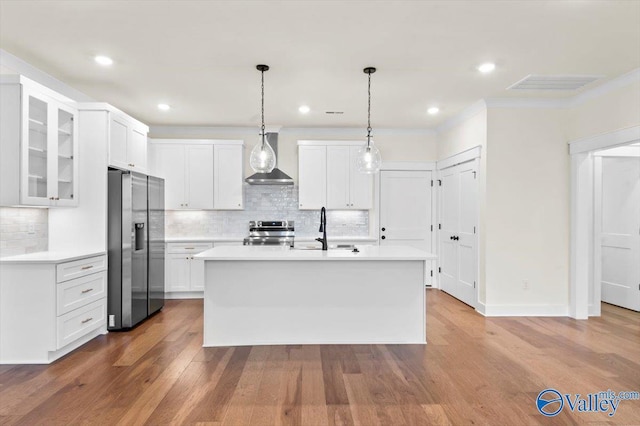 kitchen with wood finished floors, a sink, visible vents, wall chimney range hood, and appliances with stainless steel finishes