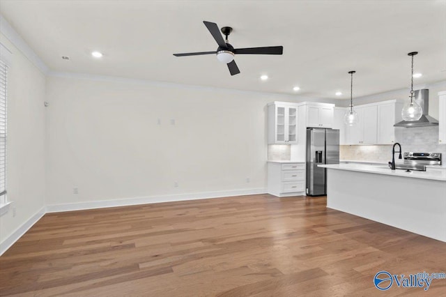 kitchen featuring stainless steel appliances, light countertops, wall chimney range hood, light wood finished floors, and tasteful backsplash