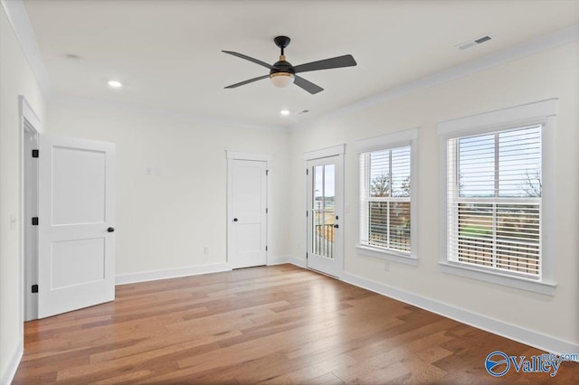 spare room featuring visible vents, crown molding, baseboards, and wood finished floors