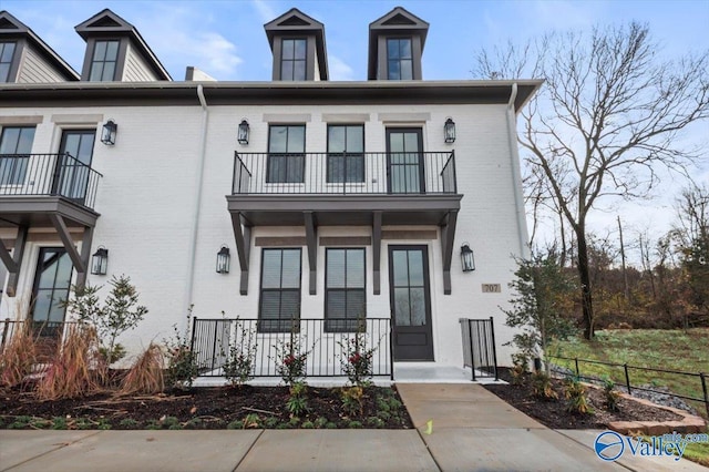 townhome / multi-family property featuring a balcony, fence, and brick siding