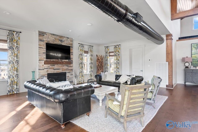 living room featuring a stone fireplace, wood finished floors, visible vents, and crown molding