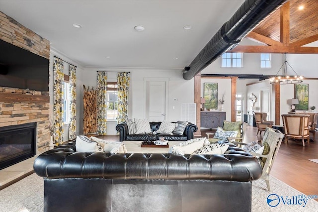 living area with a healthy amount of sunlight, an inviting chandelier, wood finished floors, and a stone fireplace