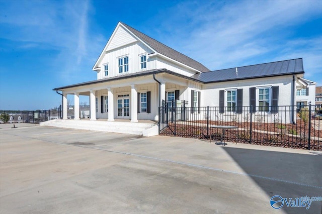 view of front of house featuring board and batten siding, metal roof, covered porch, and fence