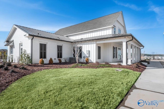 view of front of house featuring board and batten siding, a standing seam roof, a front yard, central AC, and brick siding