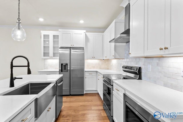 kitchen featuring light countertops, appliances with stainless steel finishes, wall chimney range hood, and decorative light fixtures