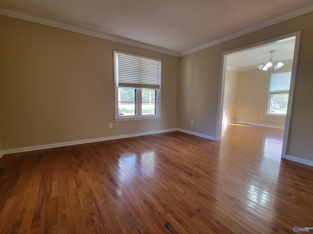 empty room featuring a chandelier, wood-type flooring, a textured ceiling, and ornamental molding