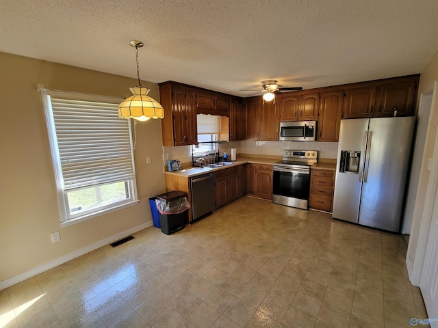 kitchen with ceiling fan, sink, stainless steel appliances, pendant lighting, and a textured ceiling