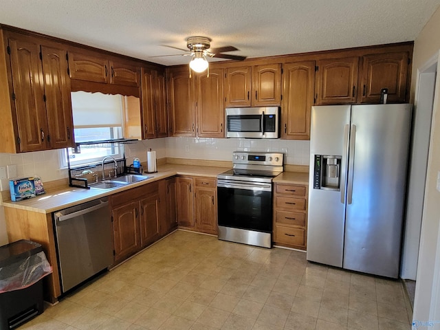 kitchen with a textured ceiling, stainless steel appliances, ceiling fan, and sink