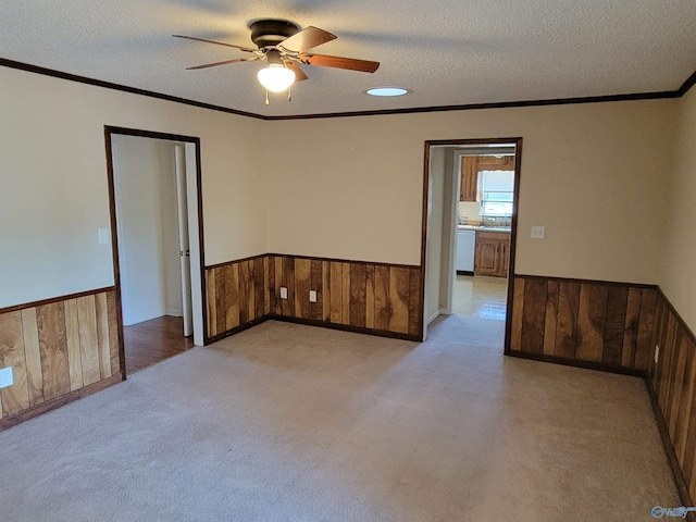 carpeted empty room featuring ceiling fan, crown molding, a textured ceiling, and wooden walls