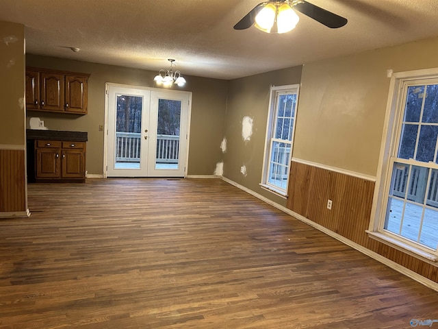 interior space with french doors, a textured ceiling, ceiling fan with notable chandelier, wooden walls, and dark wood-type flooring