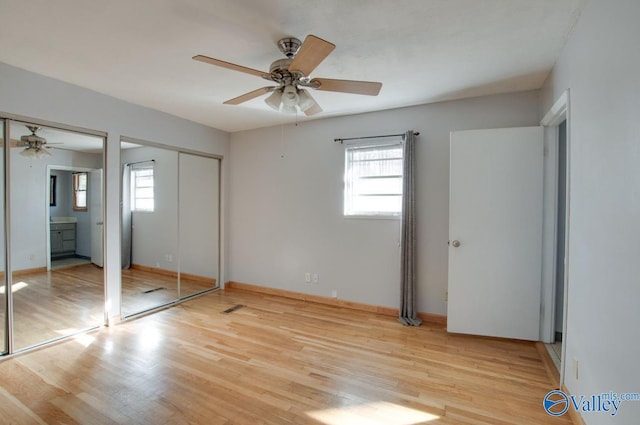 unfurnished bedroom featuring ceiling fan, multiple windows, and two closets