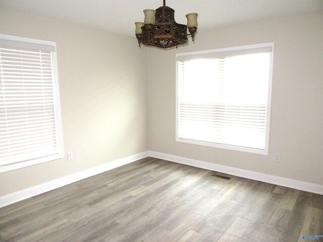 empty room with wood-type flooring and an inviting chandelier