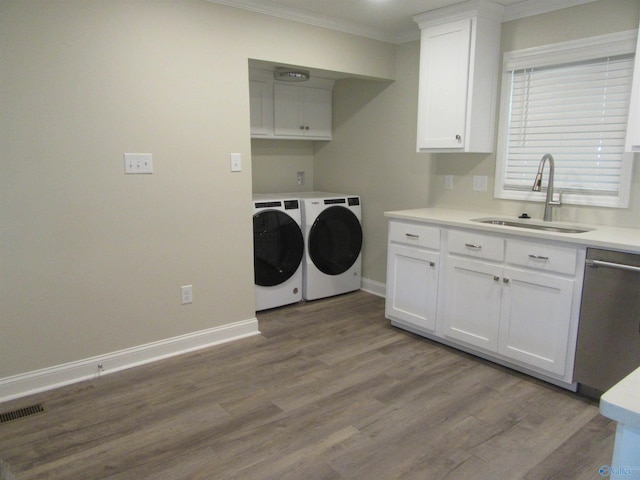 clothes washing area with washing machine and clothes dryer, crown molding, sink, and light hardwood / wood-style flooring