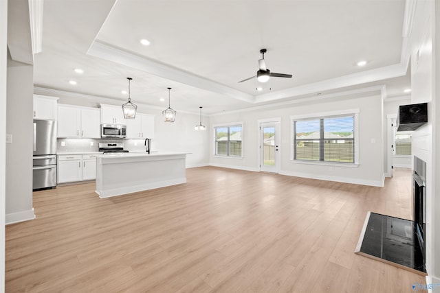 unfurnished living room with light wood-type flooring, a tray ceiling, ceiling fan, and crown molding