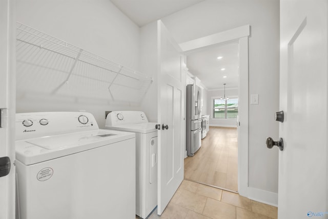 clothes washing area with washing machine and clothes dryer and light hardwood / wood-style floors