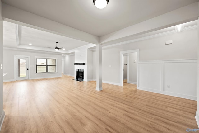 unfurnished living room with light hardwood / wood-style floors, ornamental molding, ceiling fan, a raised ceiling, and a large fireplace