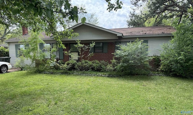 ranch-style house featuring a chimney, brick siding, and a front yard
