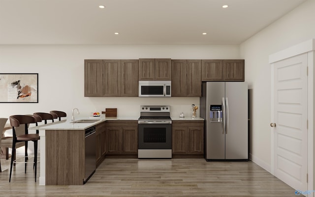 kitchen featuring stainless steel appliances, kitchen peninsula, sink, and light hardwood / wood-style flooring