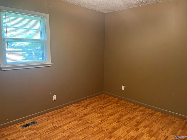 unfurnished room with light wood-type flooring and a textured ceiling