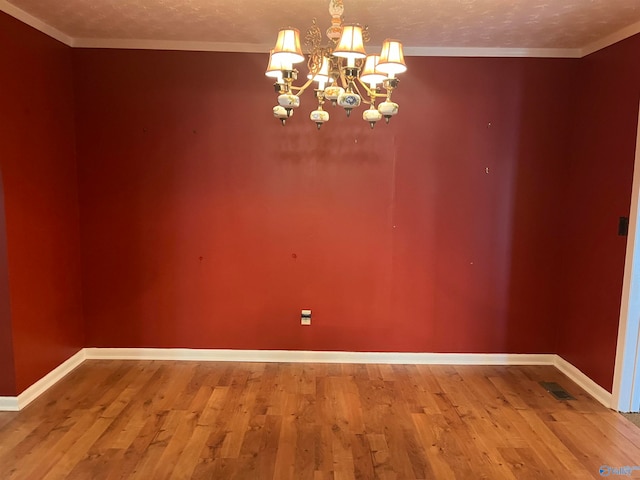 empty room featuring a textured ceiling, crown molding, wood-type flooring, and a chandelier