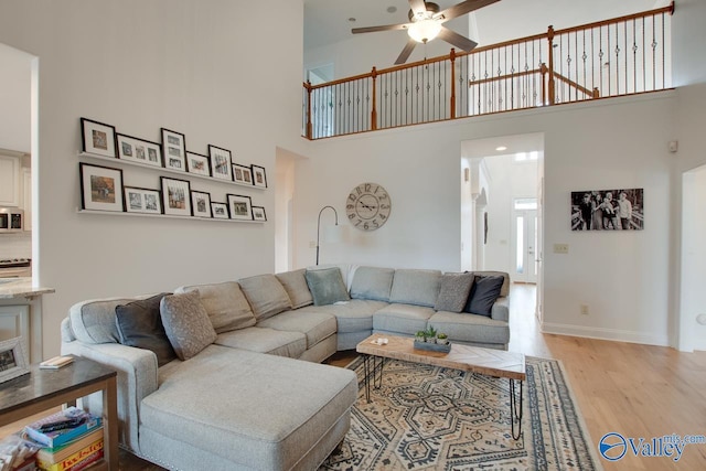 living room featuring ceiling fan, a towering ceiling, and light hardwood / wood-style floors