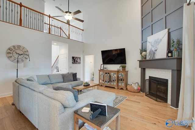 living room featuring a brick fireplace, a towering ceiling, light hardwood / wood-style floors, and ceiling fan