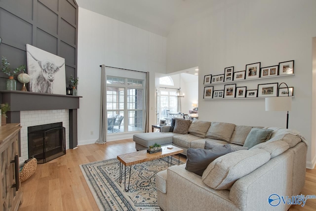 living room with a towering ceiling, a brick fireplace, and light hardwood / wood-style flooring