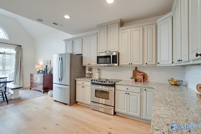 kitchen with white cabinetry, vaulted ceiling, light hardwood / wood-style flooring, appliances with stainless steel finishes, and light stone countertops