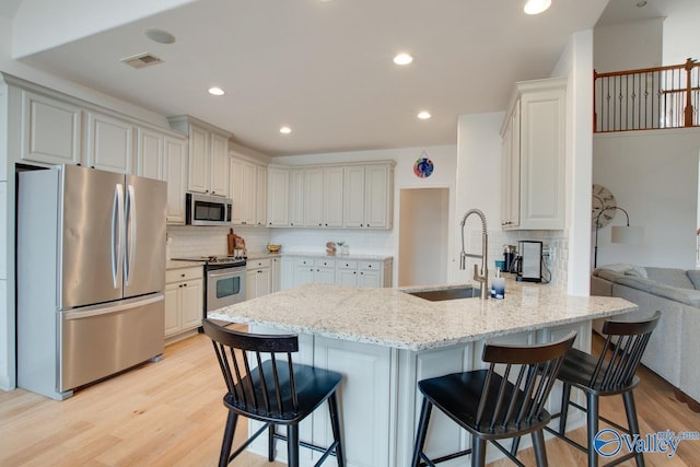 kitchen with sink, light stone counters, appliances with stainless steel finishes, a kitchen breakfast bar, and kitchen peninsula